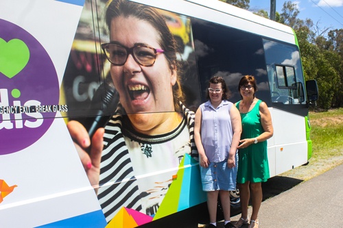 Steph and her mum stand next to a bus that features a giant picture of a happy Steph singing